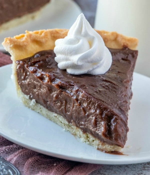 Chocolate pie topped with whipped cream on a white plate.
