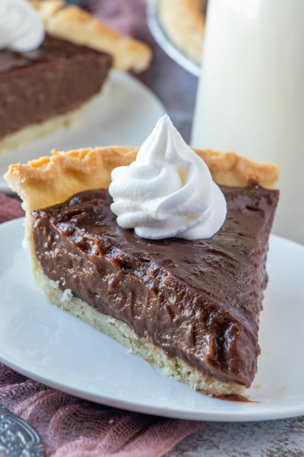 Old Fashioned Chocolate Pie slice on a white plate topped with whipped cream. 