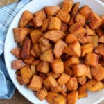 Cinnamon and Brown Sugar Sweet Potatoes in a white bowl on wooden cutting board with blue dish towel and spoon