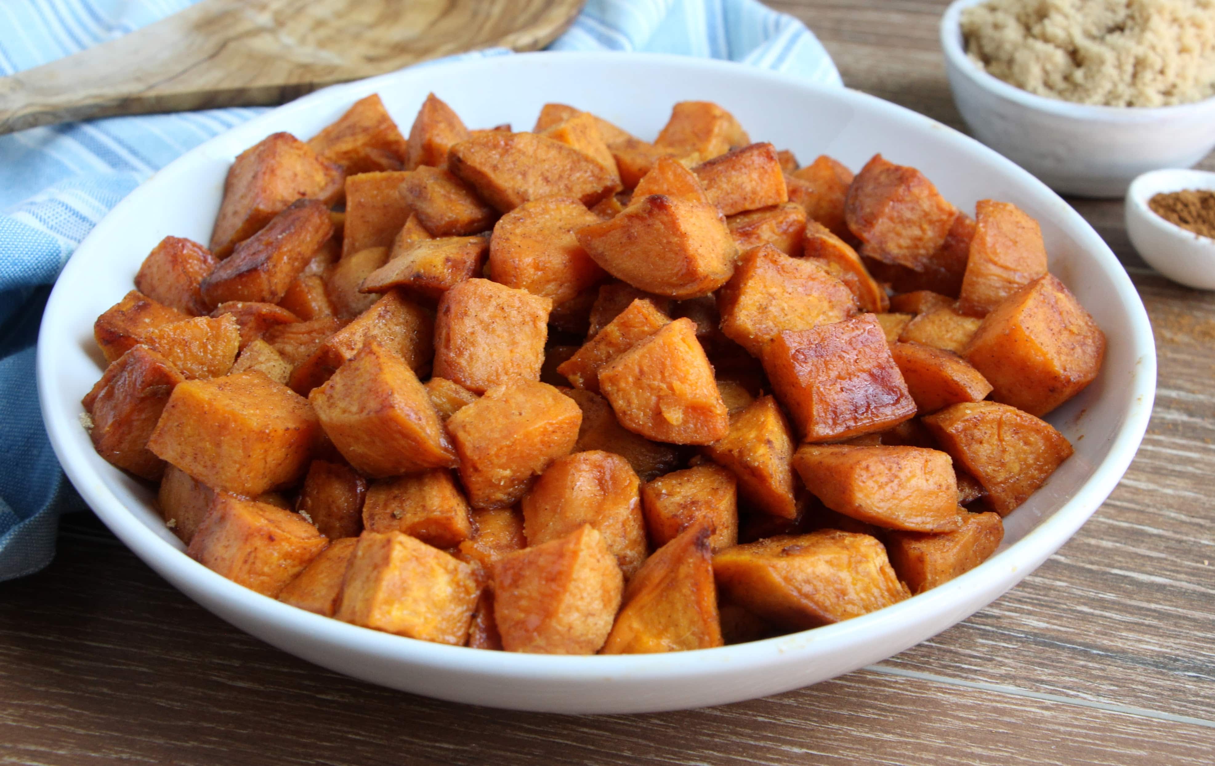 Roasted Cinnamon and Brown Sugar Sweet Potatoes in a white bowl sitting on a wooden cutting board
