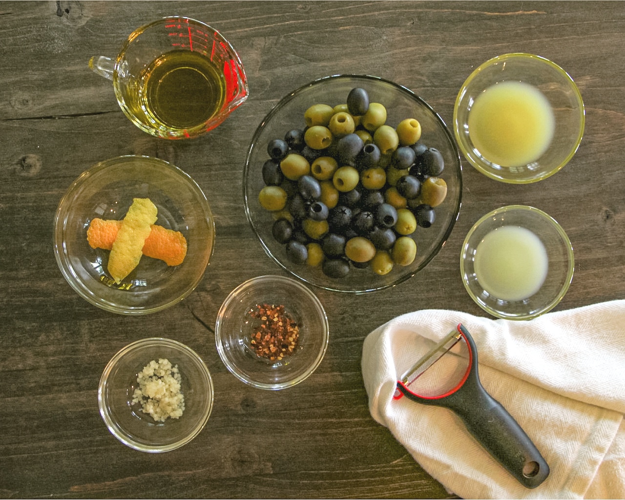 Ingredients needed to make Citrus Marinaded Olives on a wood cutting board.