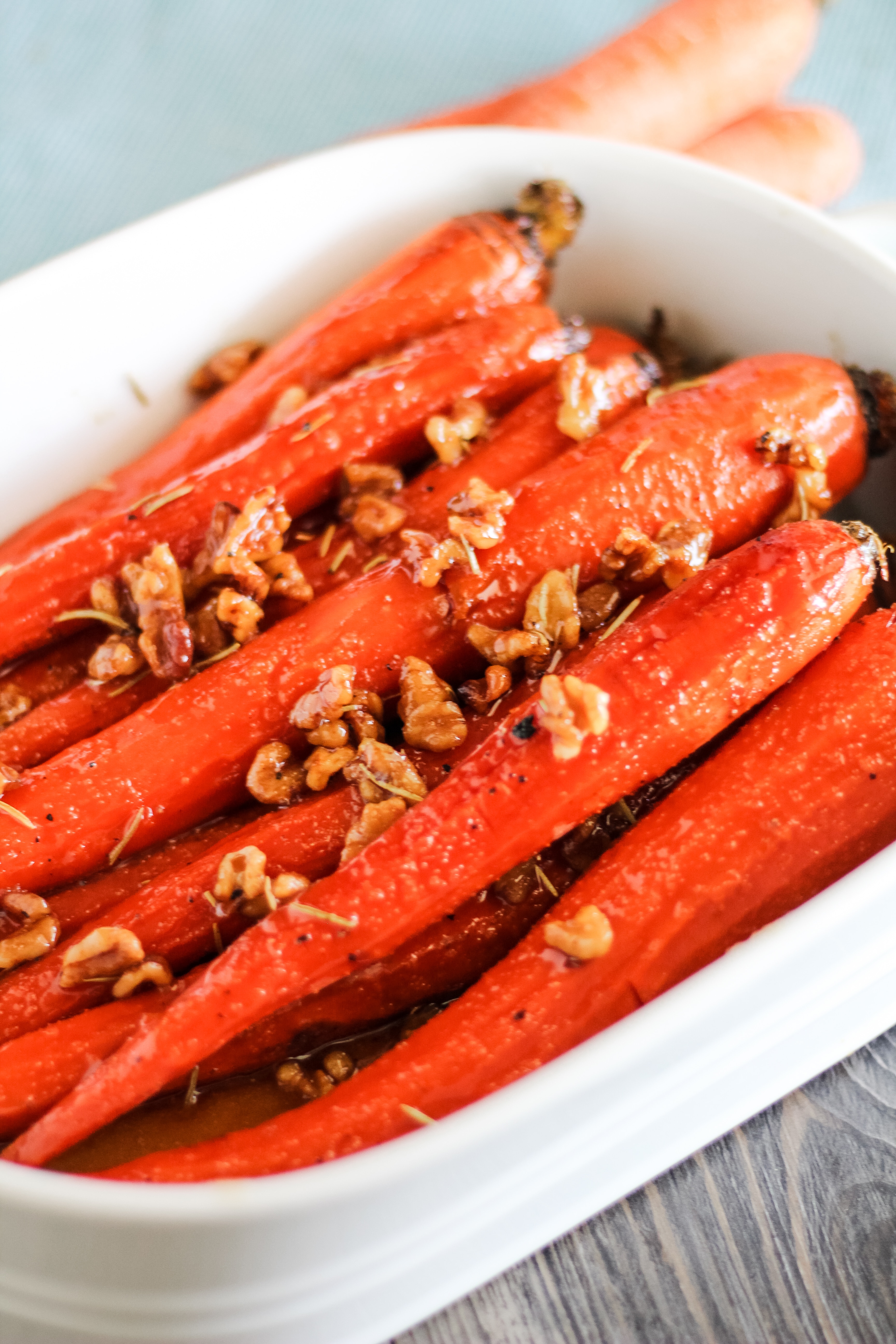 Honey and Maple Glazed Carrots in a garnished with walnuts and rosemary in white serving dish