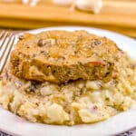 Pork Chop smothered in gravy sits on a bed of mashed potatoes.