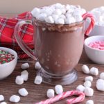 A mug of hot cocoa with marshmallows and a candy cane