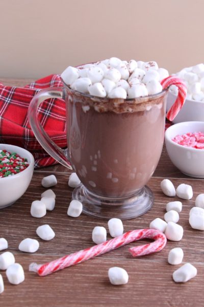 A mug of hot cocoa with marshmallows and a candy cane