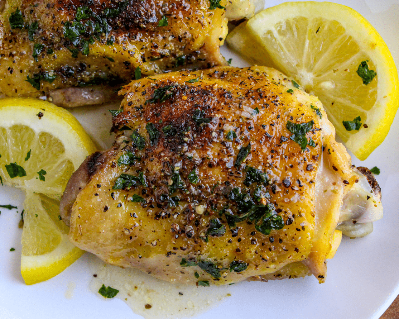Lemon Pepper Chicken Thighs and lemon slices on a white plate garnished with chopped parsley 