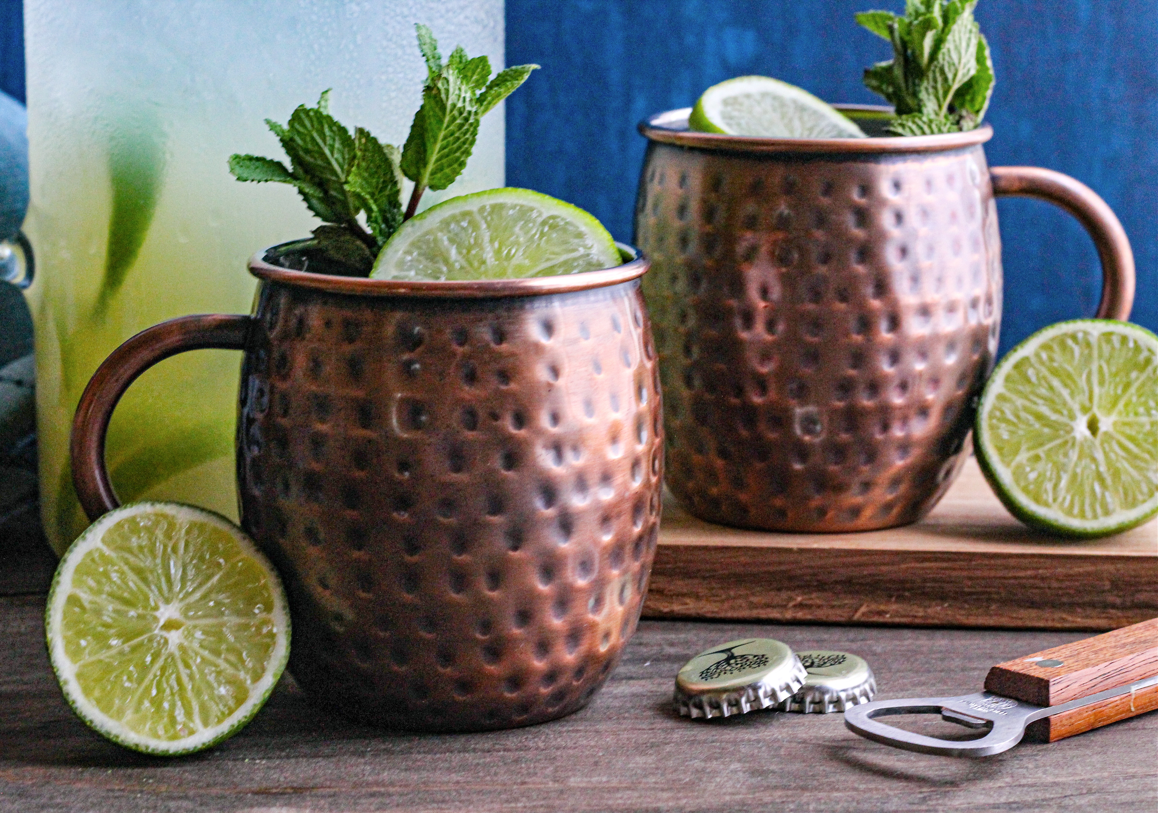 Two Moscow Mules in copper mugs garnished with limes and mint.