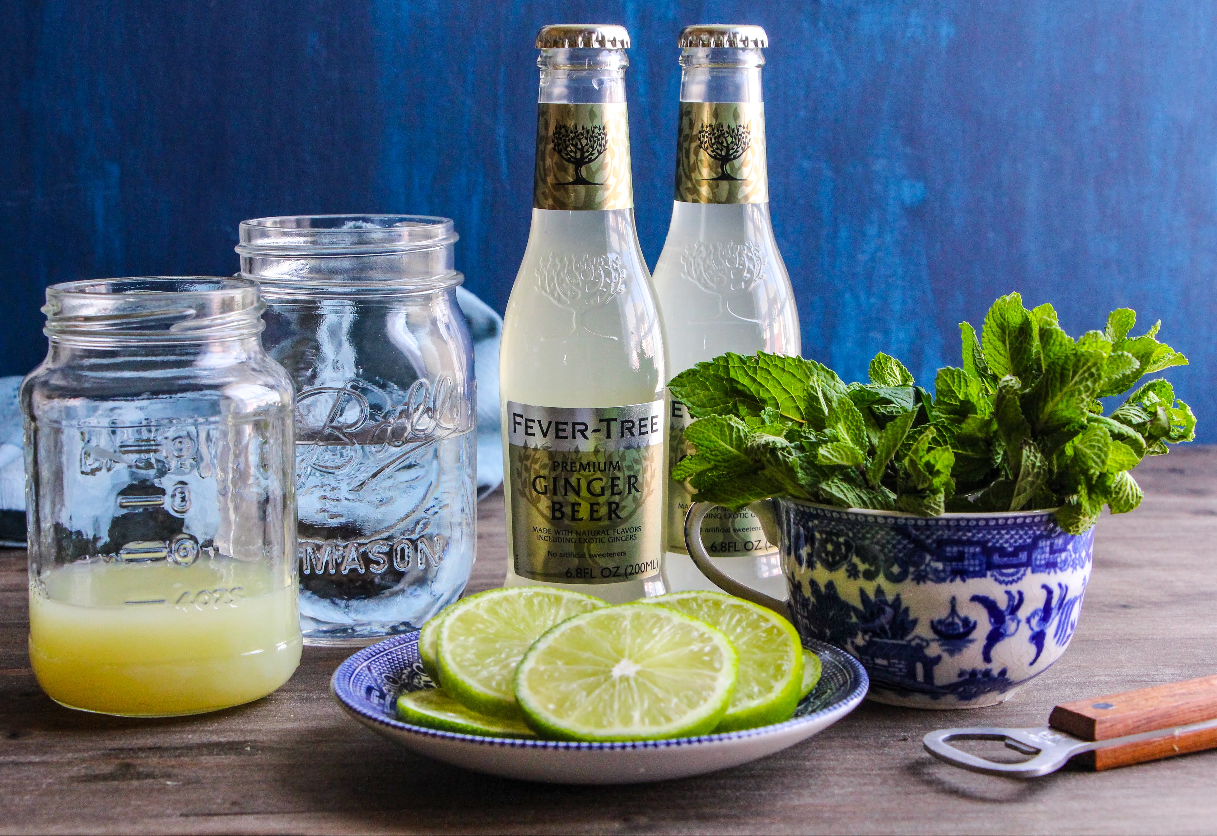 Jars with lime juice and vodka next to two bottles of Ginger beer and fresh mint. 