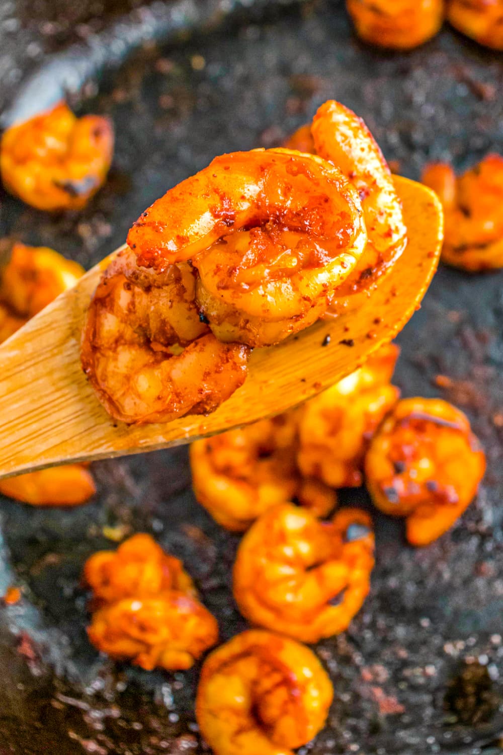 Prepared Chipotle seasoned shrimp on a wooden spoon being scooped from the skillet. 