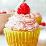 A single lemon cupcake with raspberry frosting topped with a fresh raspberry on a white background.