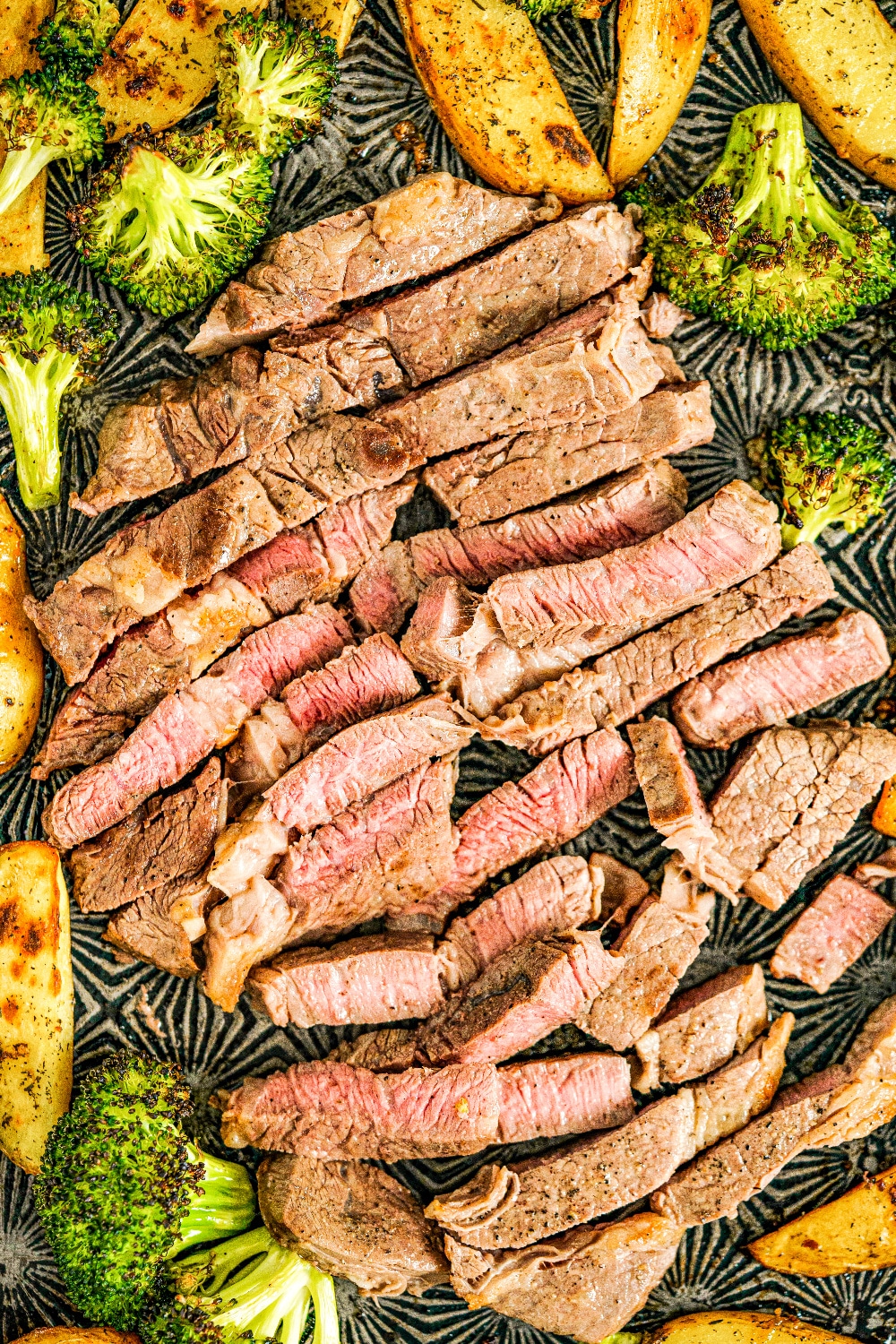 Sliced steak surrounded by broccoli and potatoes on a sheet pan.