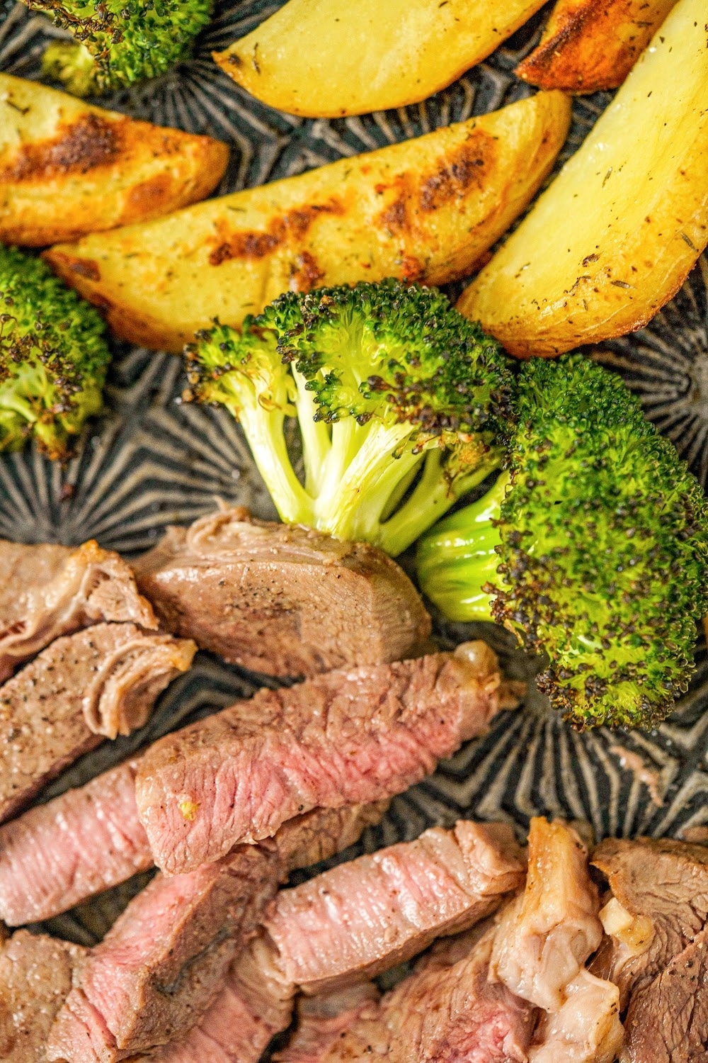 Golden potatoes, broccoli and sliced steak on a sheet pan.