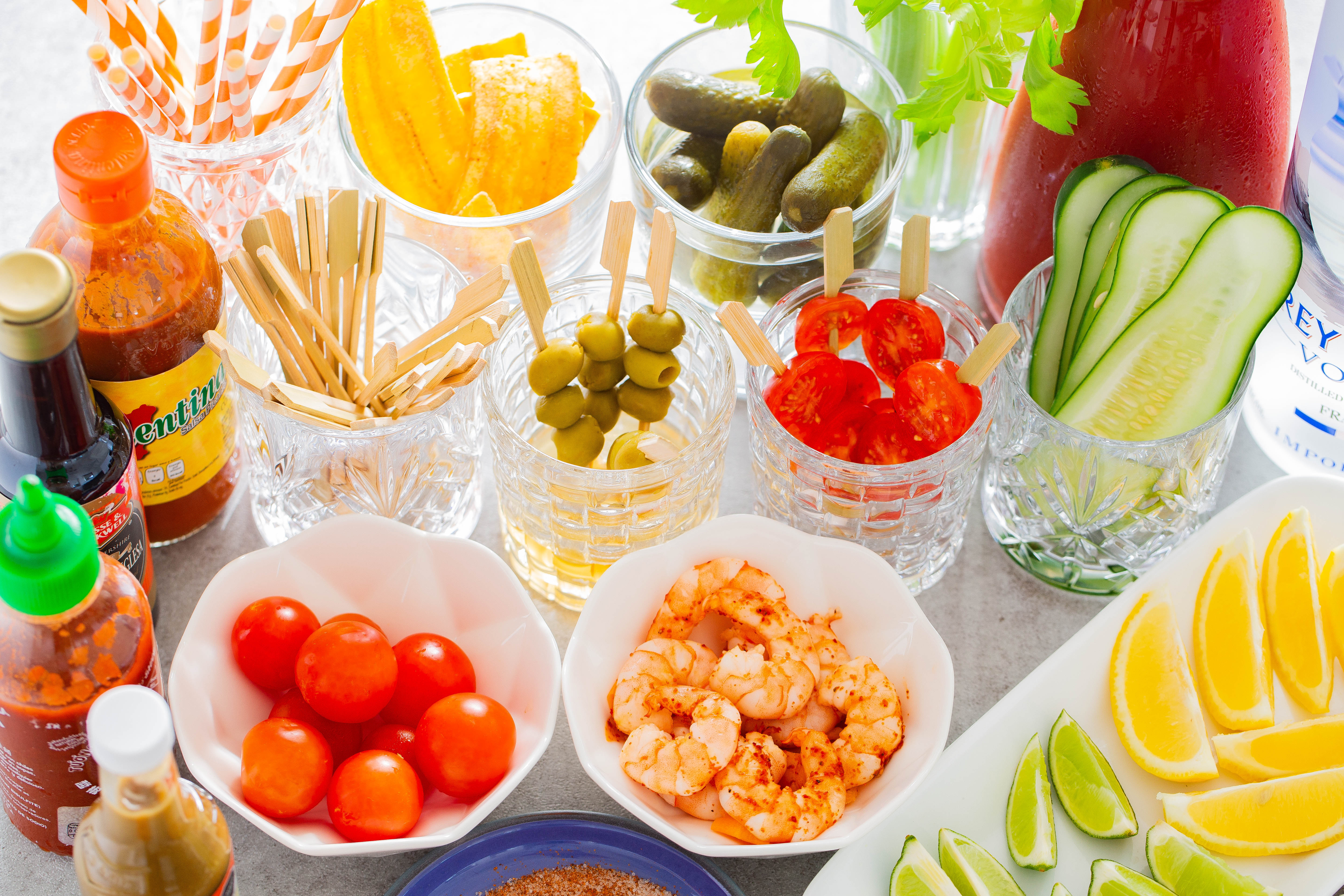 Straws, kosher pickles, celery, Bloody Mary mix, dill pickles, cherry tomatoes, olives and shrimp played out in clear bowls to create a Bloody Mary Bar.