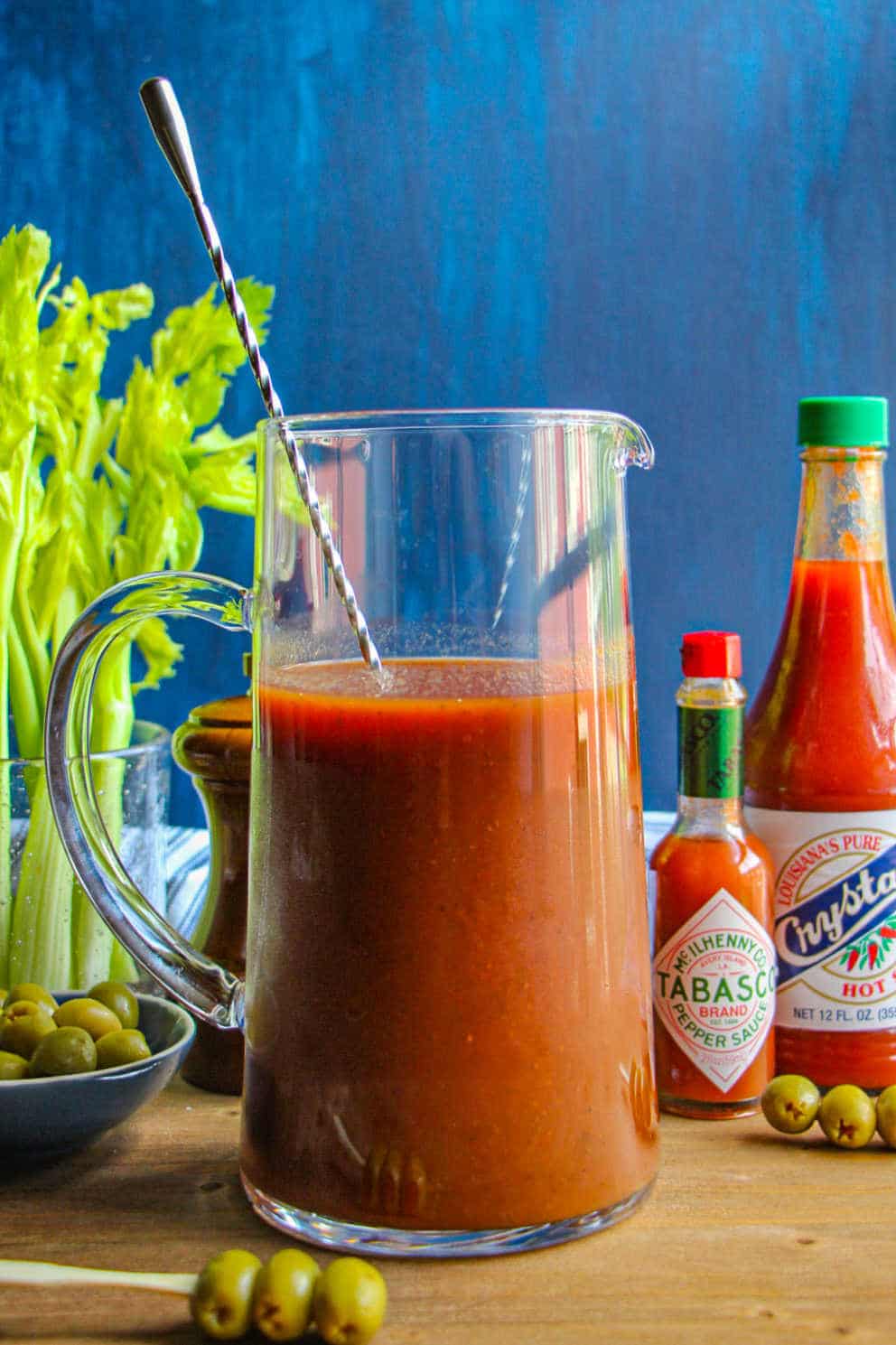 Bloody Mary Mix in a clear glass pitcher with a cocktail spoon.