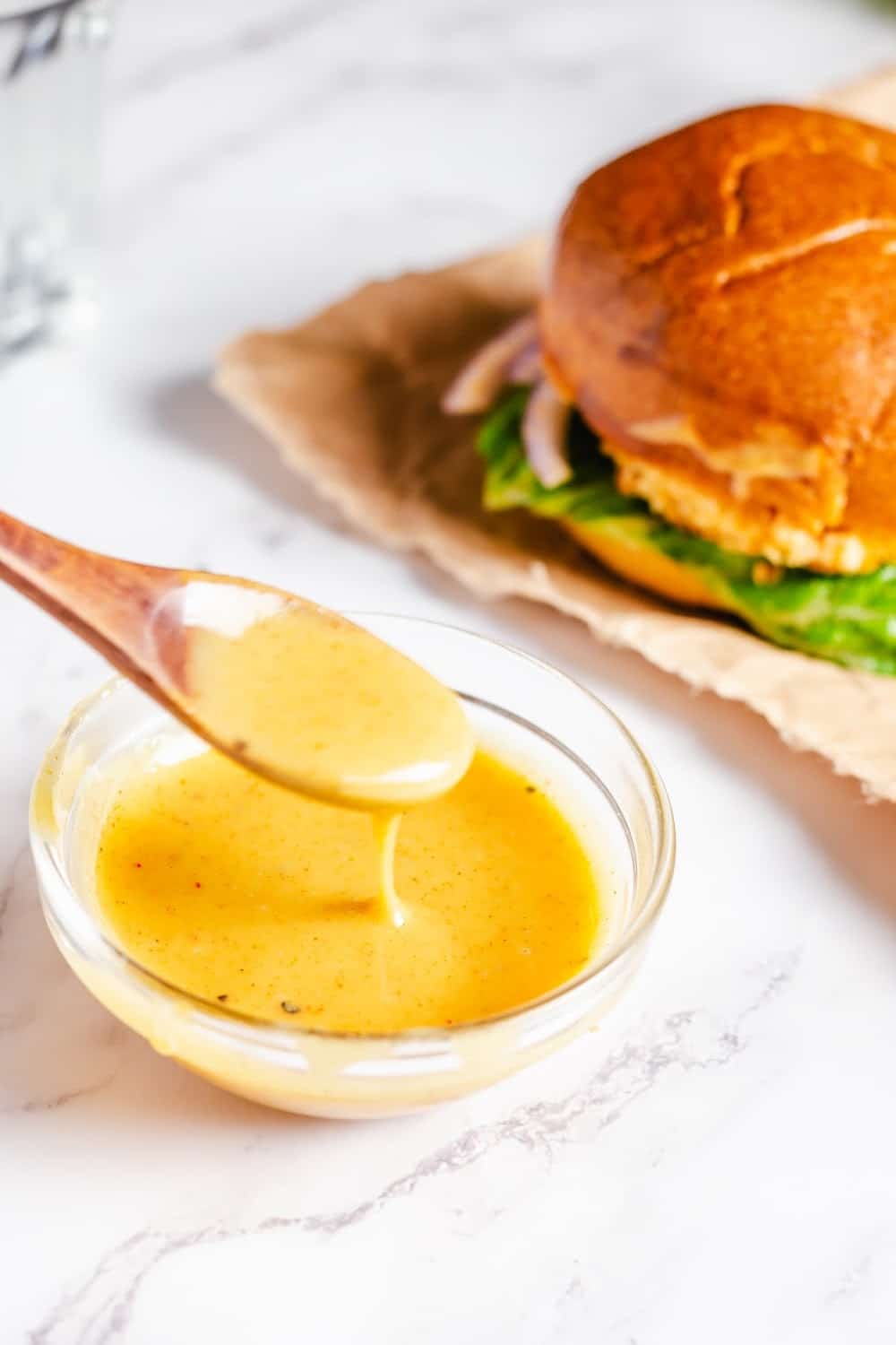 A spoonful of Honey Mustard Sauce over a clear glass bowl.