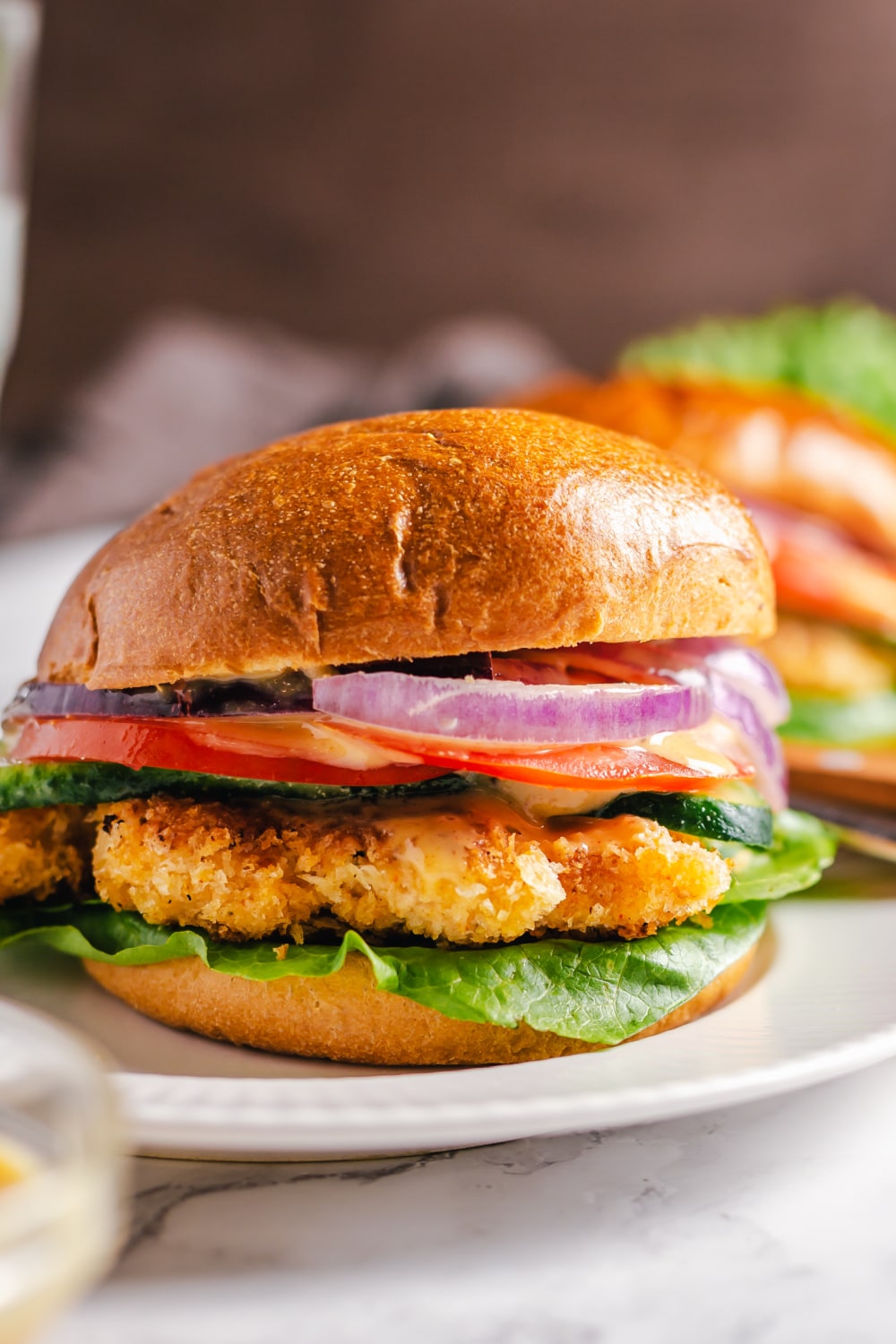 Crispy Chicken Sandwich garnished with red onion, tomatoes and lettuce on a white plate.