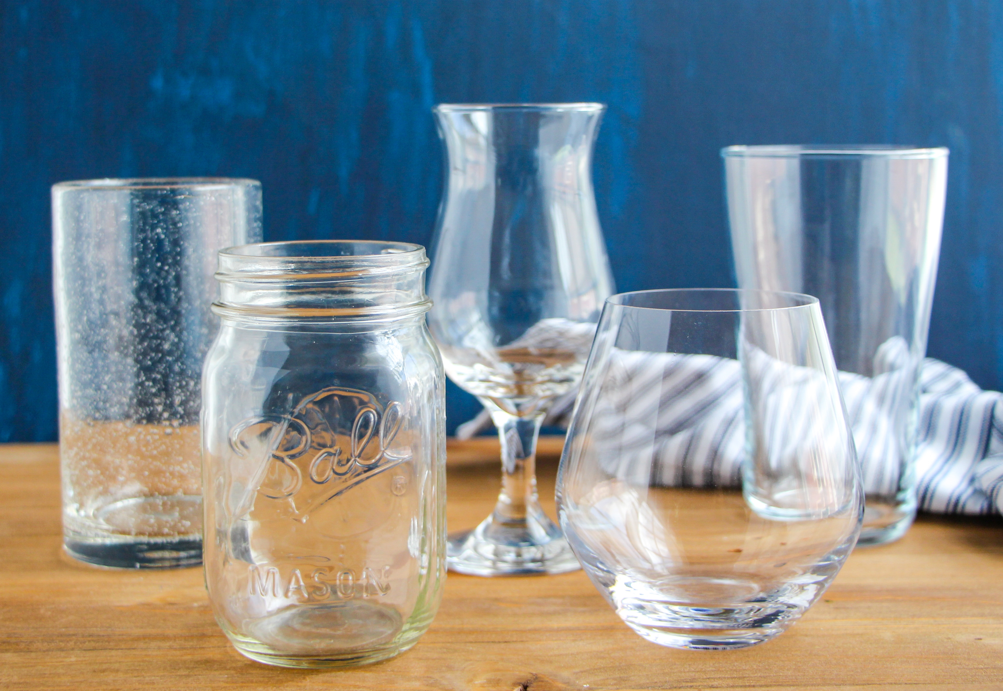 Empty drinking glass, mason jar, cocktail glass, stemless wine glass, rocks glass on a wooden tabletop.