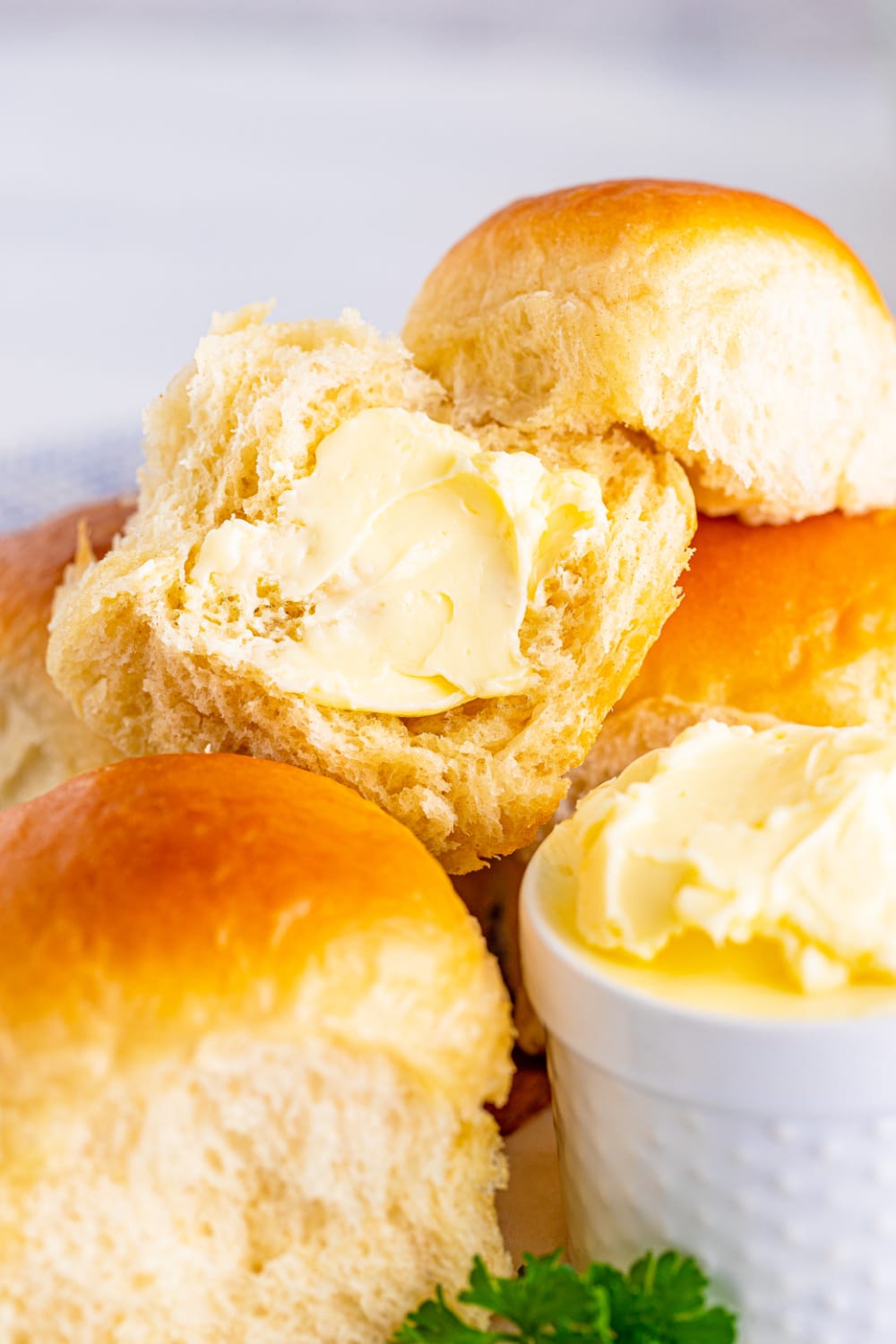 Dinner rolls on a platter with one sliced opened and smeared with butter.