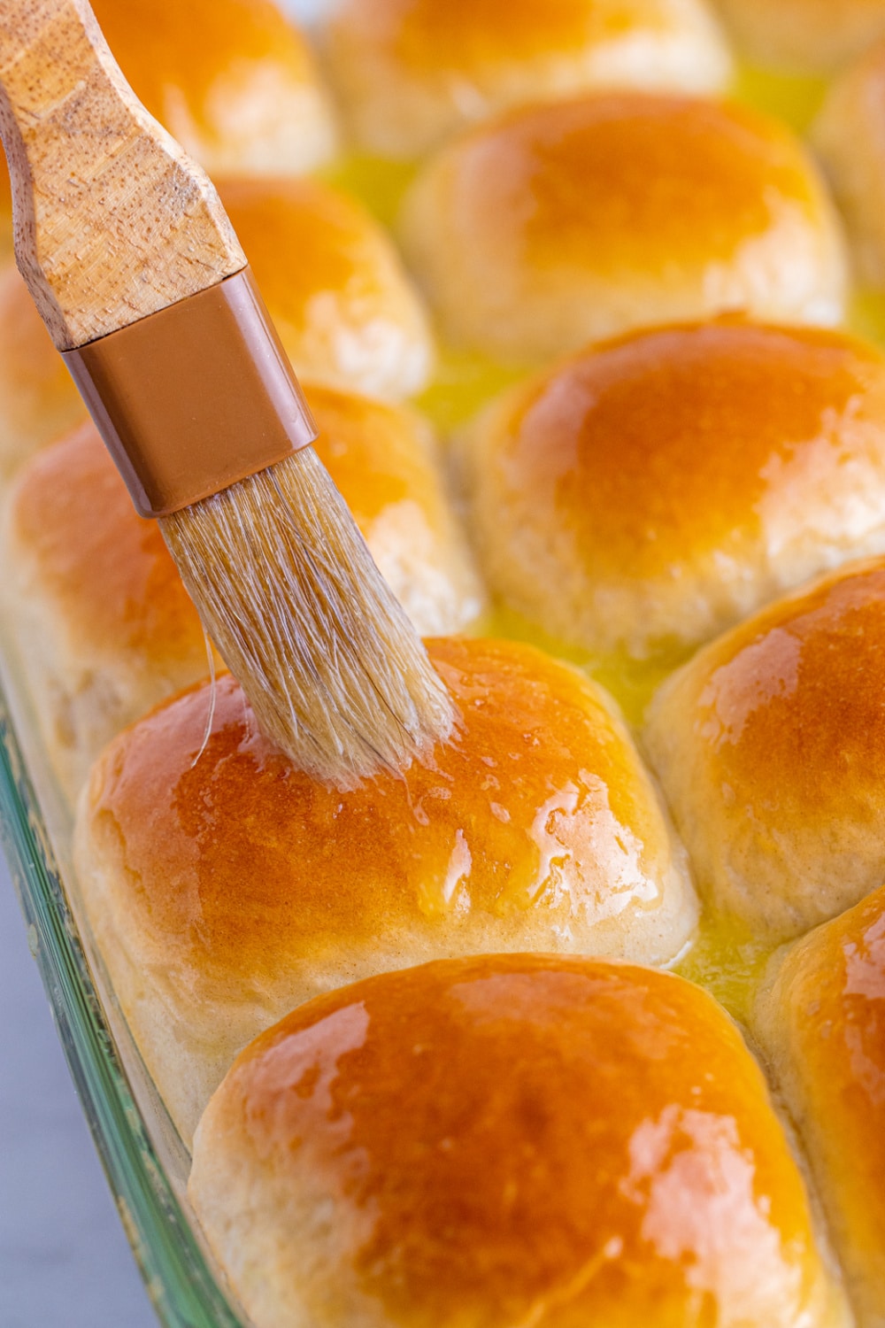Rolls in a glass baking dish bring brushed with butter.