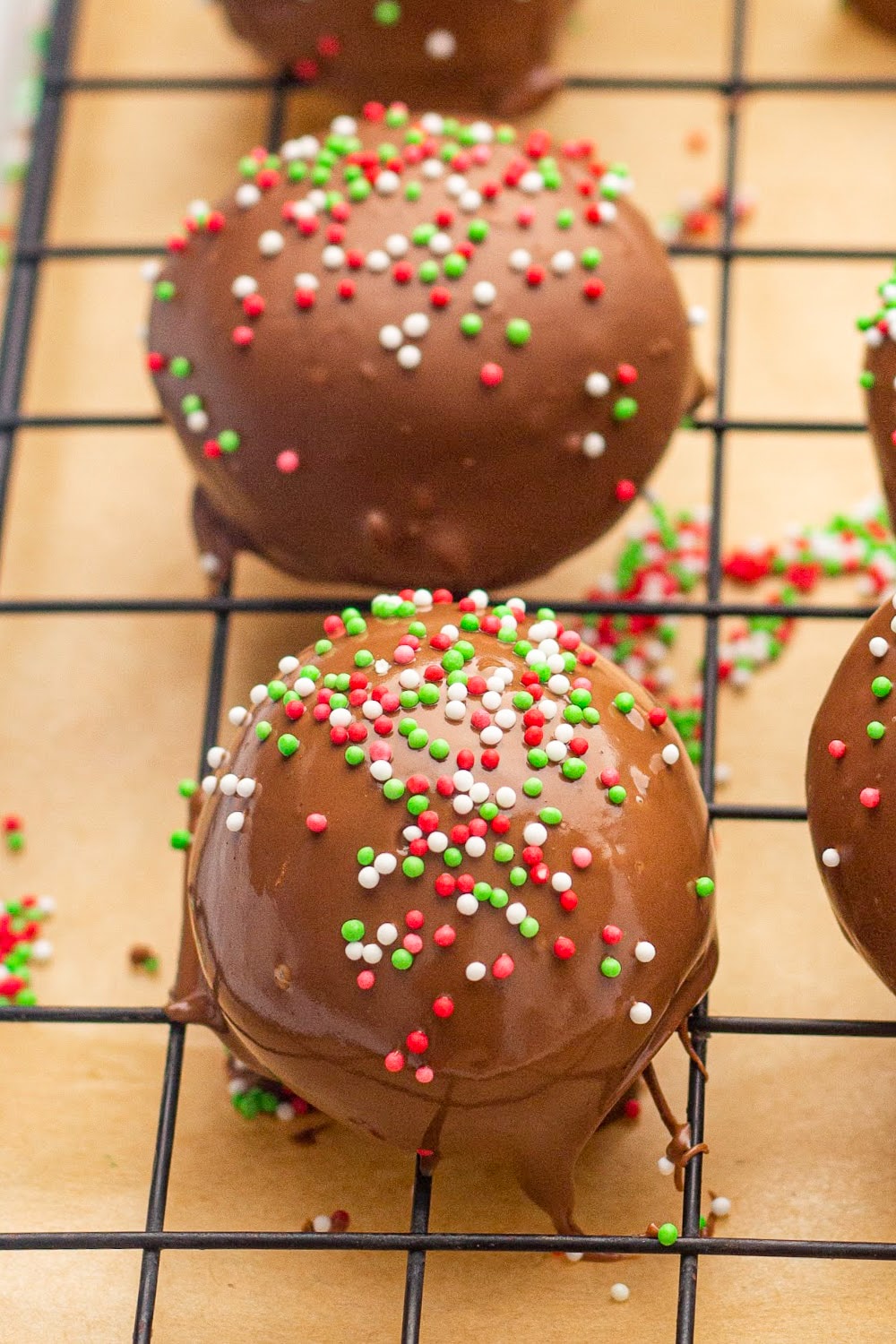 Truffles on a rack drizzled in milk chocolate and topped with red, green and white sprinkles.