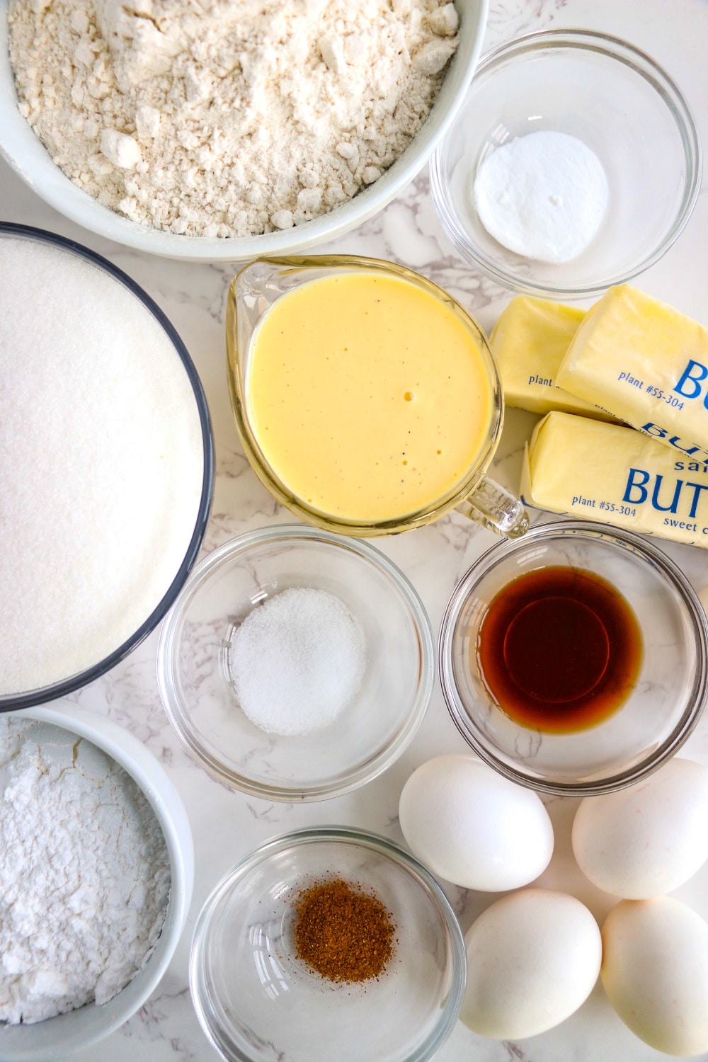 Measured ingredients needed to make Eggnog Bundt Cake in bowls on white background.