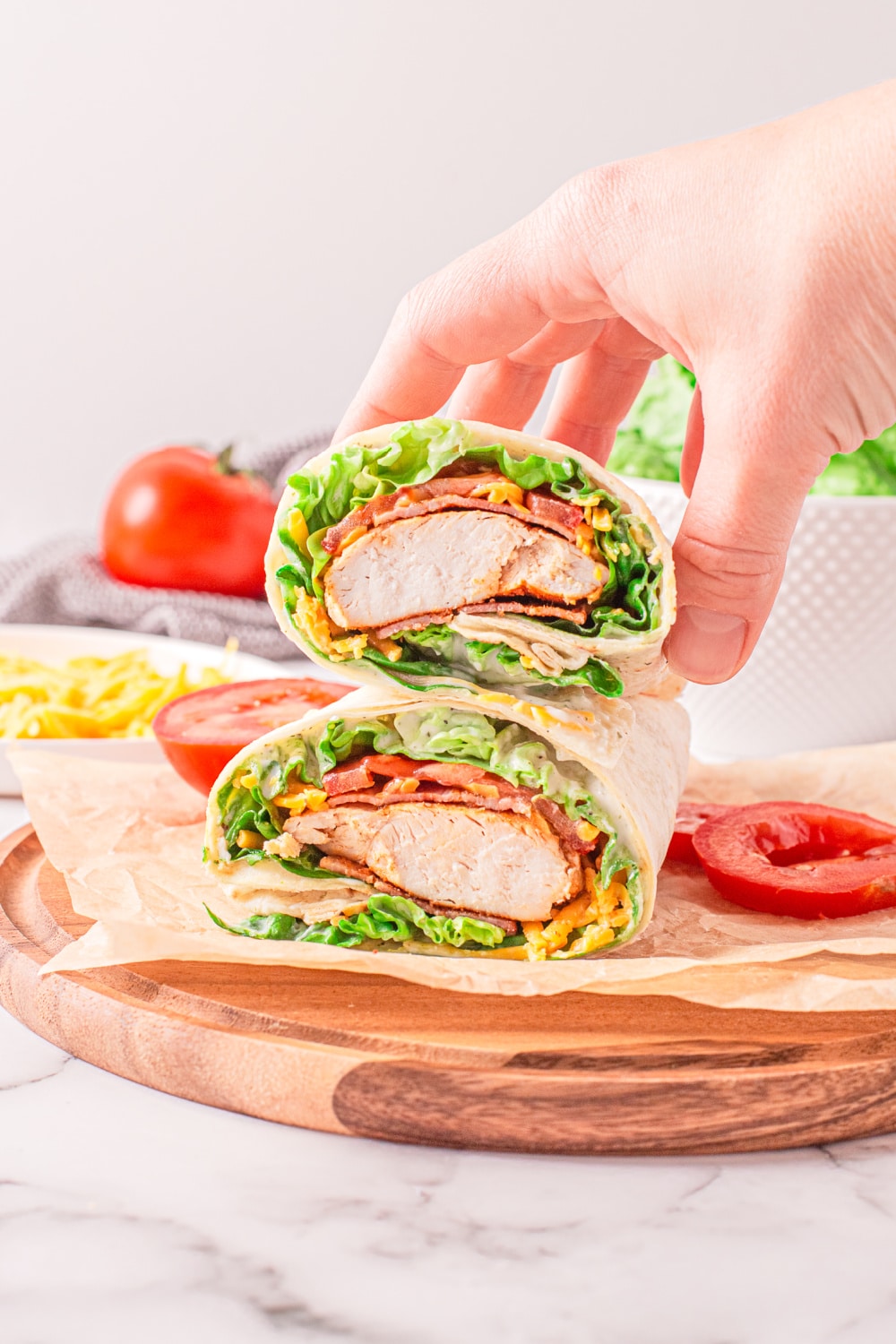 A woman's hand reaches to pick up a prepared wrap sitting on a wood cutting board.