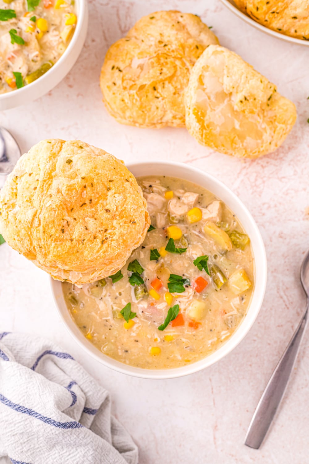 Chicken Pot Pie Soup in a white bowl with a puff pastry biscuit on the side. 