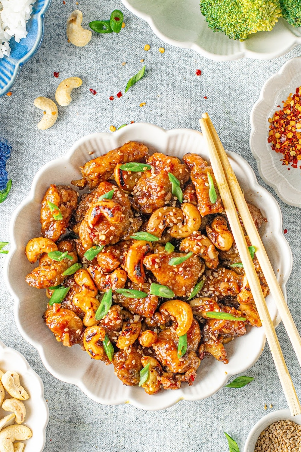 Cashew Chicken garnished with sesame seeds and scallions in a white bowl with chopsticks resting on the edge.