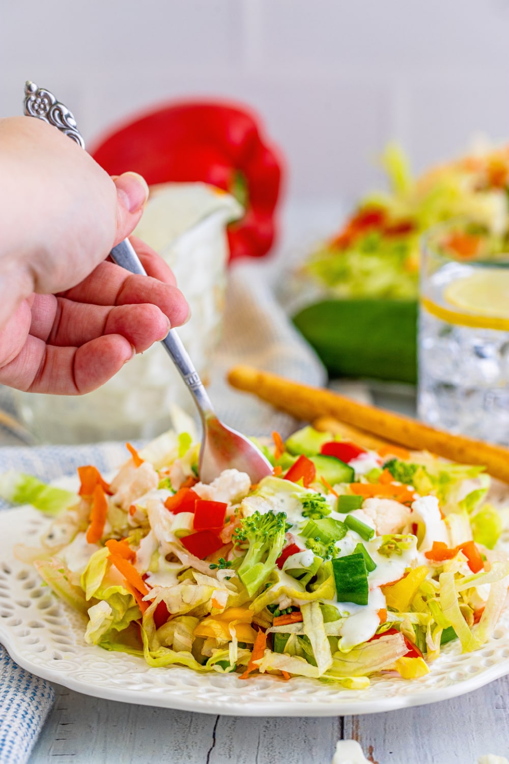 A female hand holds a fork stabbing a bite of salad from a white plate.