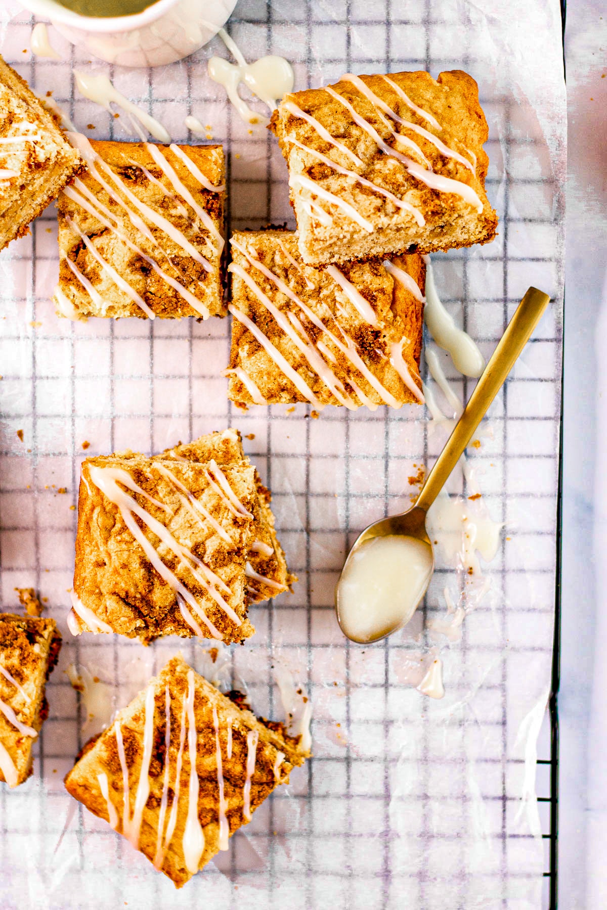 Squares of blondies on a cooling rack sitting next to a gold table spoon filled with cream cheese icing mixture. 