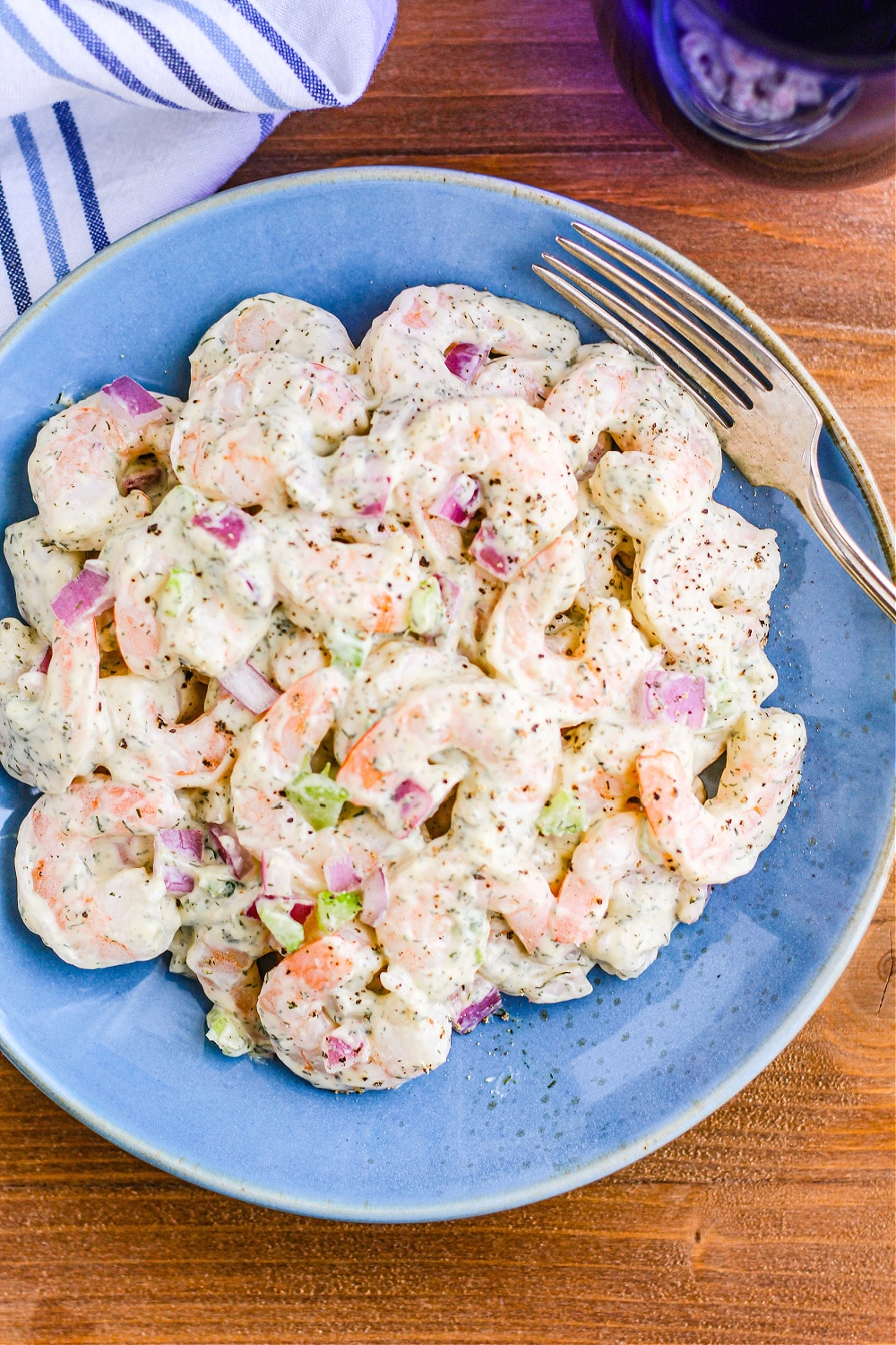 Shrimp Salad on a blue plate next to a fork and blue water glass.