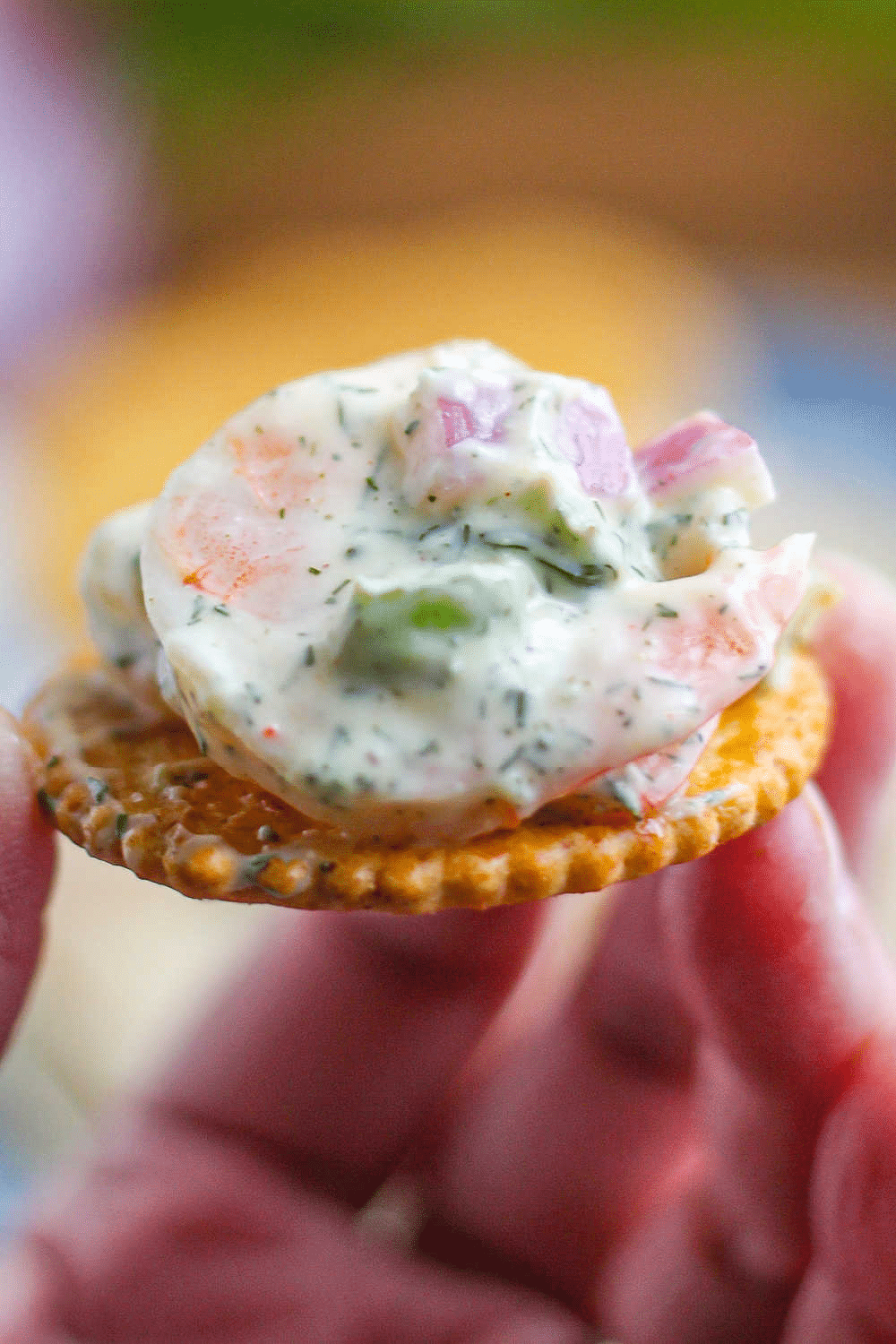 A woman's hand holding a cracker topped with shrimp salad. 
