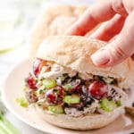 A woman's hand placing the top bun on a chicken salad sandwich.