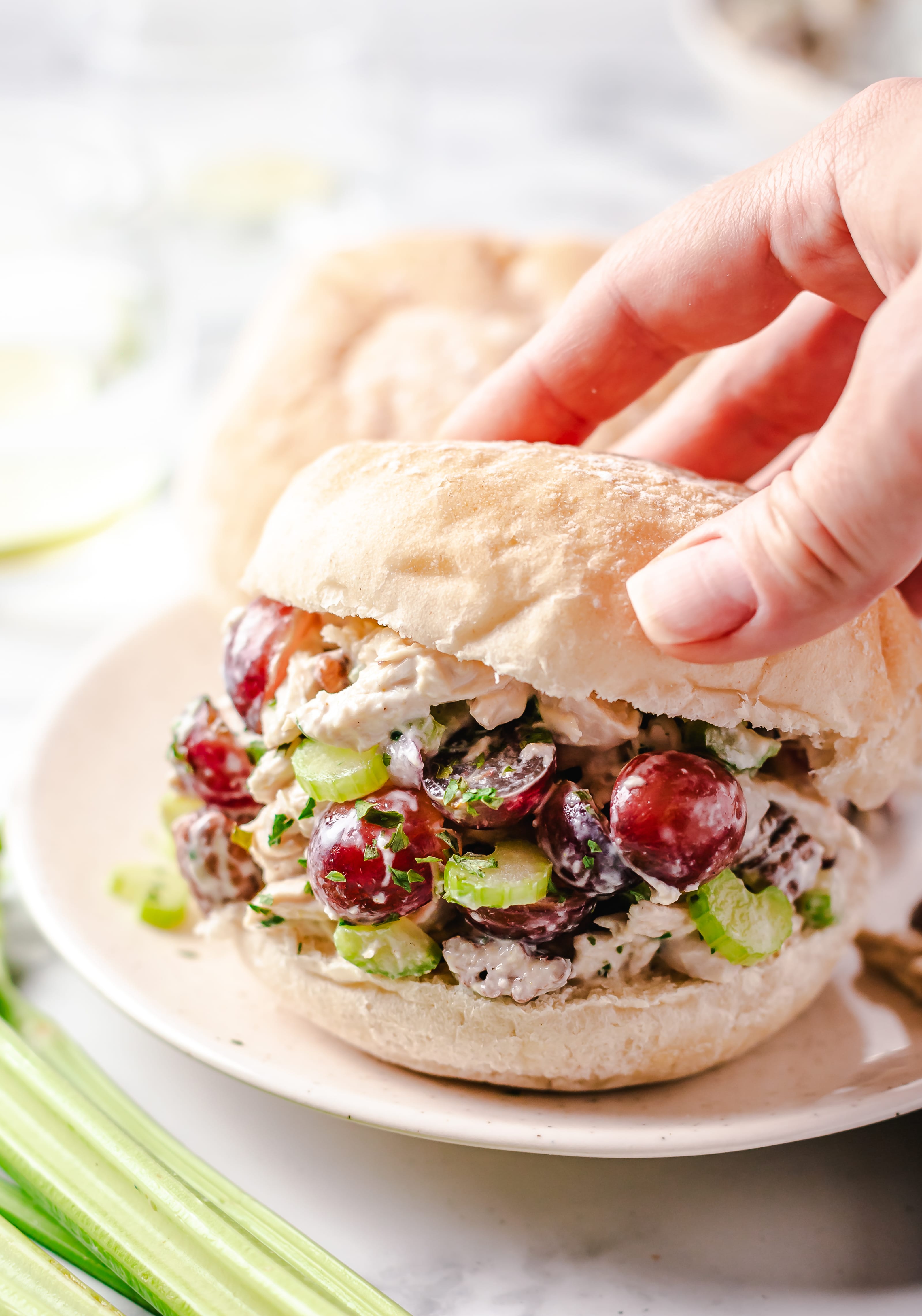 A woman's hand placing the top bun on a chicken salad sandwich.