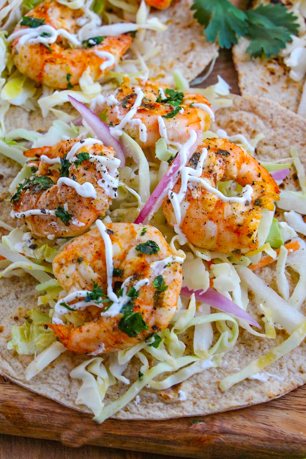Seasoned Shrimp laying on a tortilla with slaw and red onions.