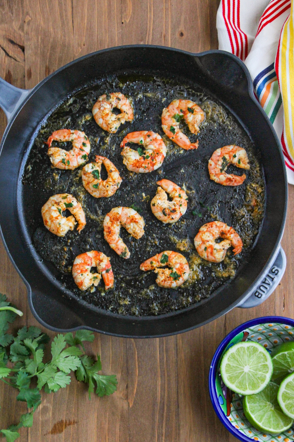 Prepared shrimp in large skillet sitting next to a striped towel and a bowl of limes.