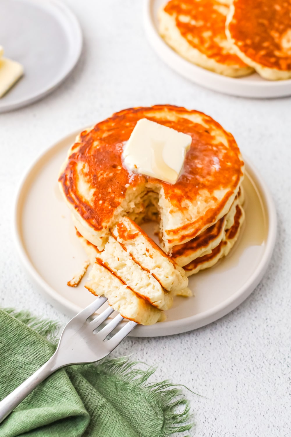 A stack of three pancakes topped with a pat of butter with a bite cut out on a fork.