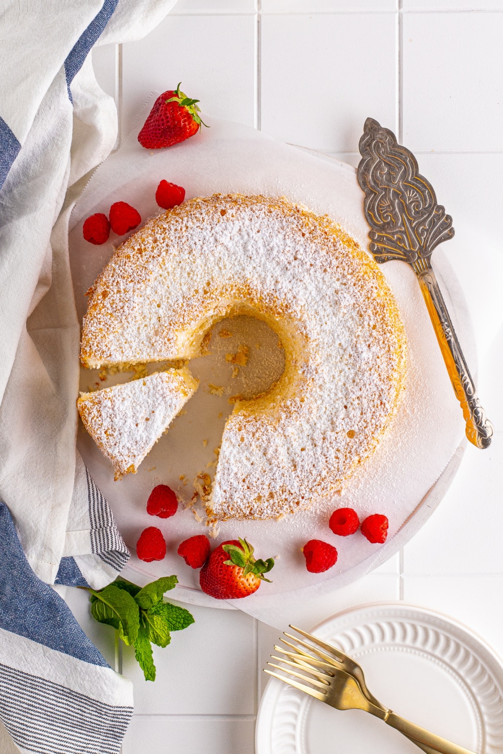 Angel Food Cake dusted with powdered sugar and cake server sitting on a white platter with.