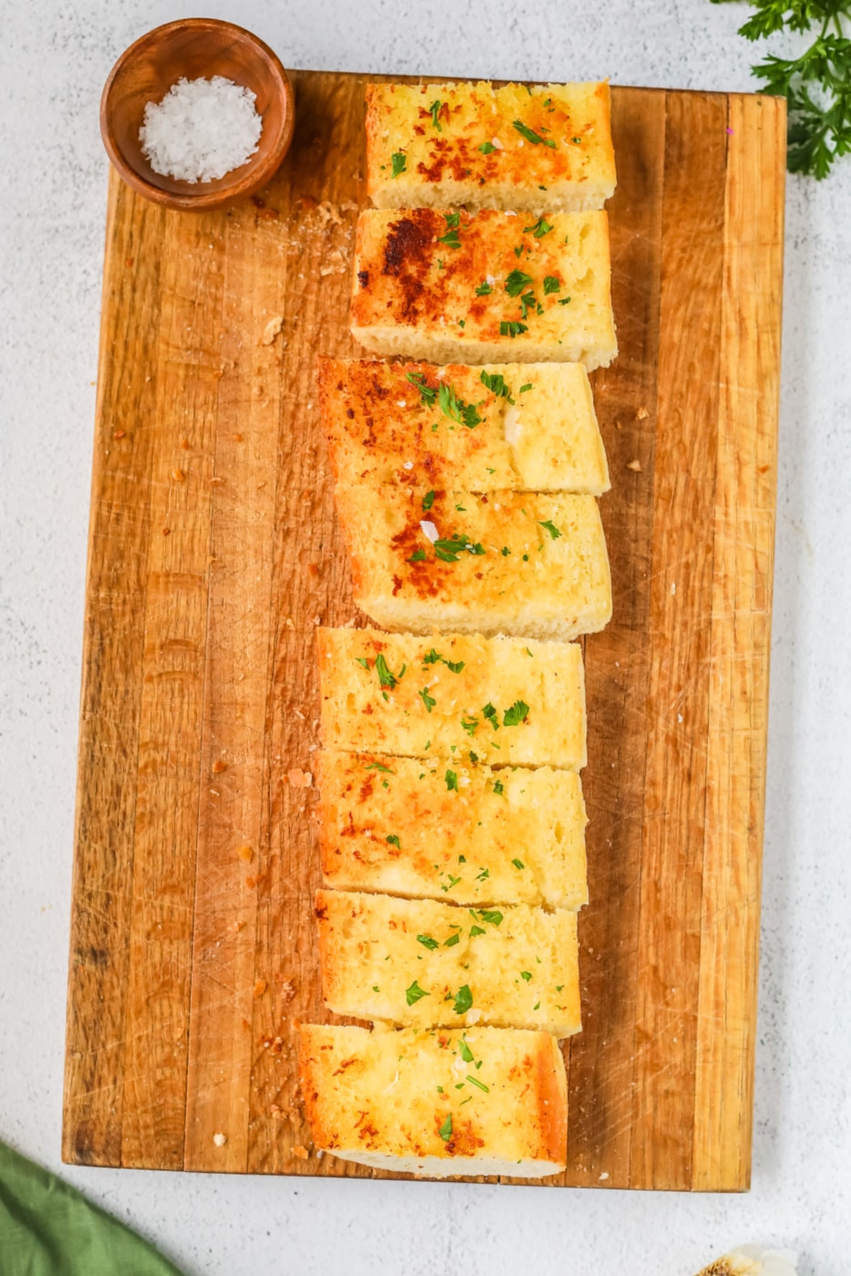 Sliced garlic bread garnished with chopped parsley on a wood cutting board.