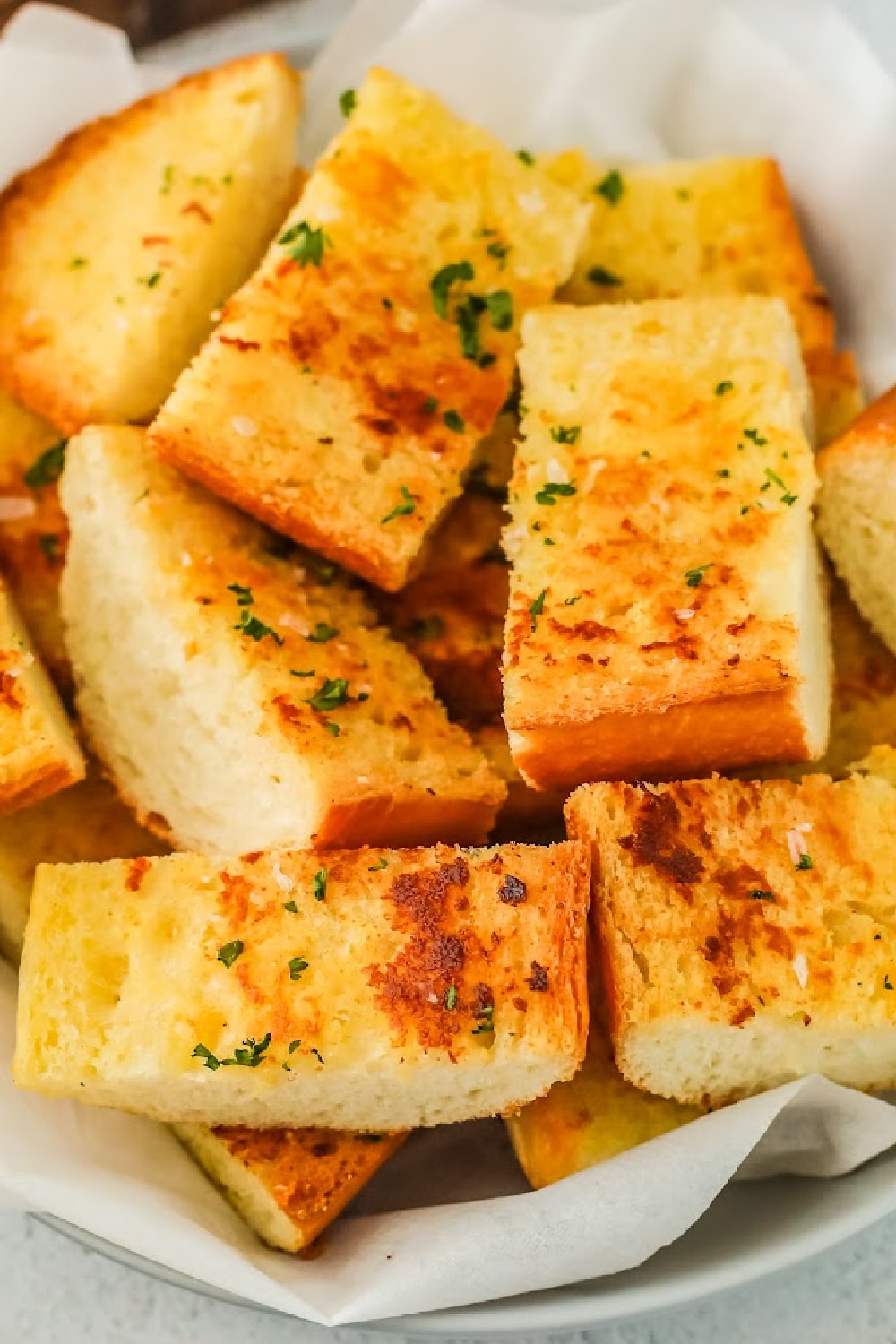Garlic bread in a basket lined with white parchment paper.