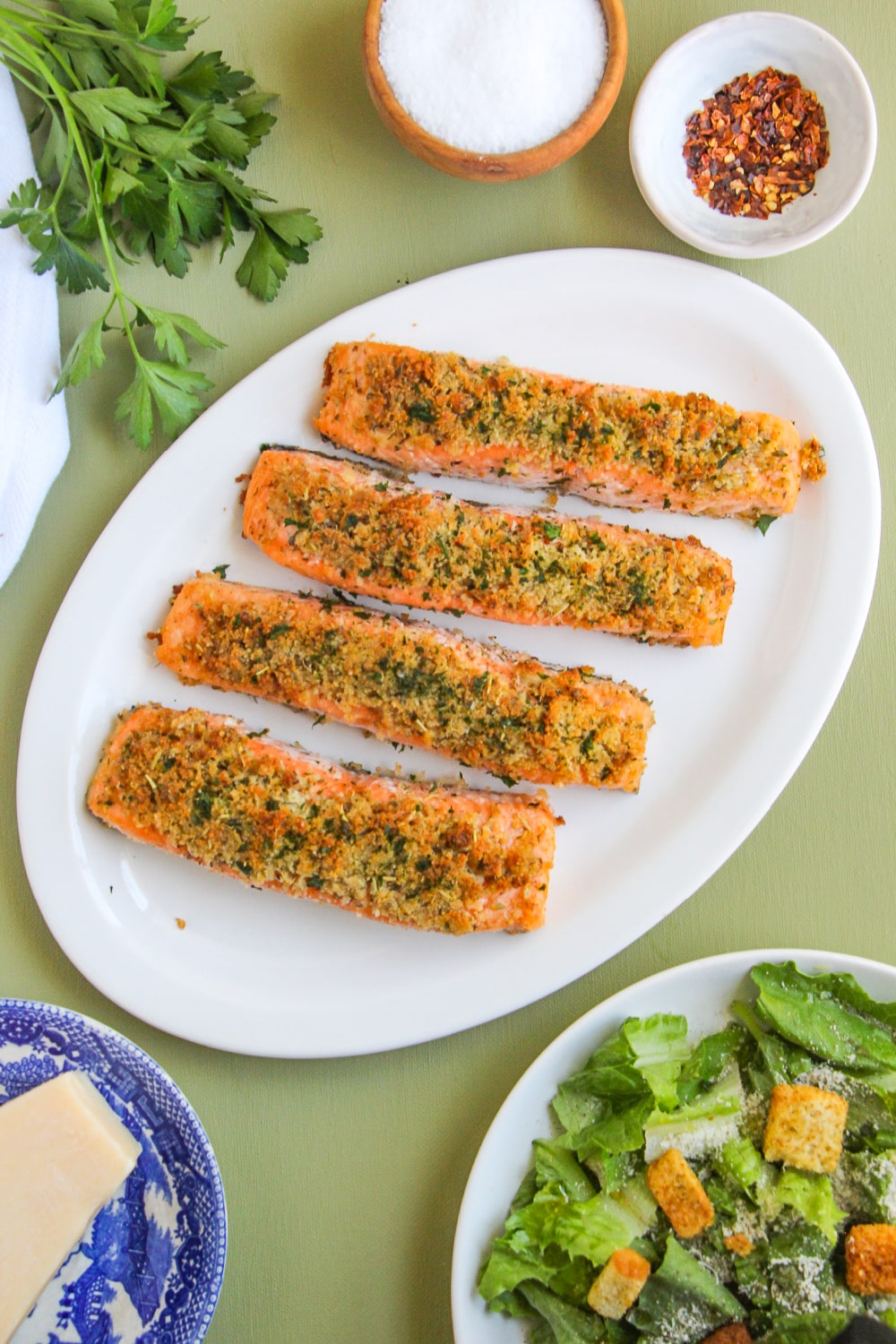 Four Garlic Parmesan Salmon fillets on a white platter sitting on a green background.