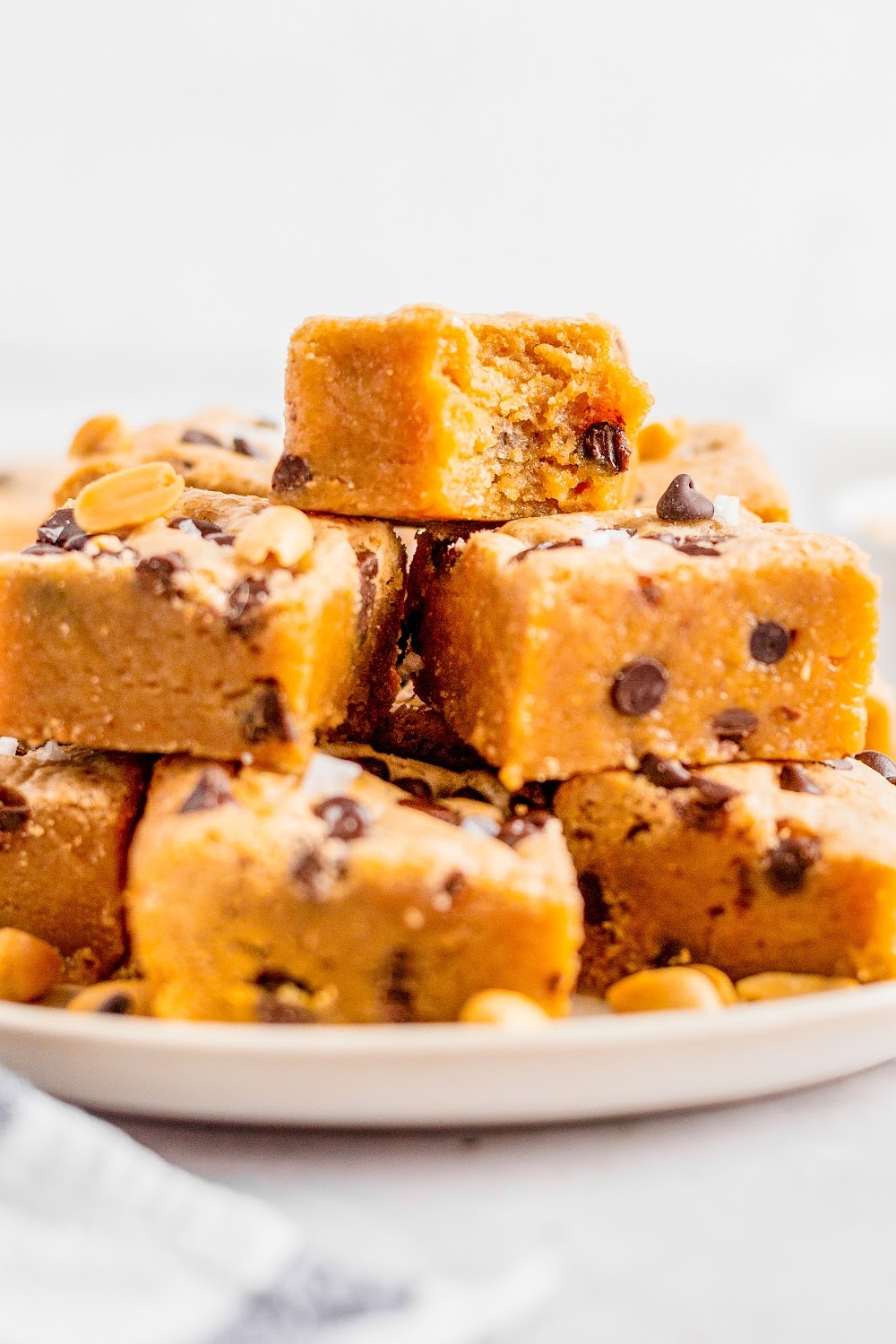 A stack of peanut butter chocolate chip blondies on a white plate the top blondie has a bite missing.