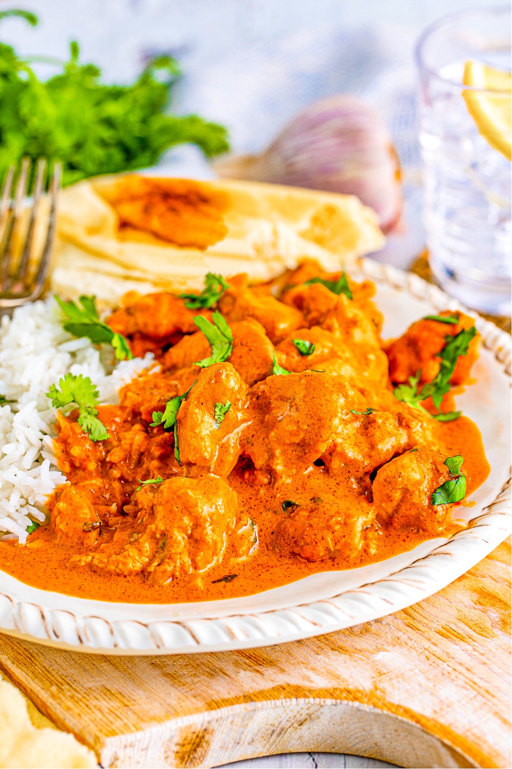 A serving of Butter Chicken with Naan on a white plate rests on a wood table top. 
