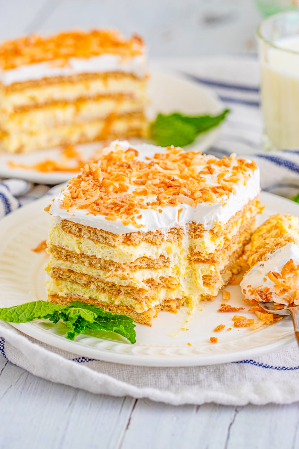 Two slices of Coconut Icebox Cake topped with toasted coconut on white dessert plates.