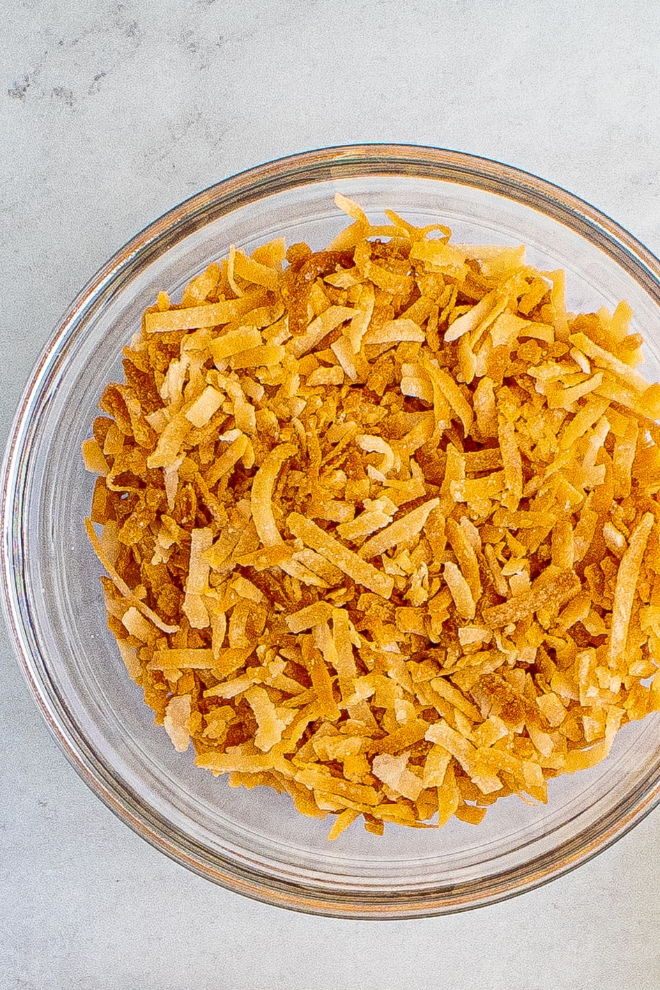 A clear glass bowl of toasted coconut flakes on a white marble countertop.