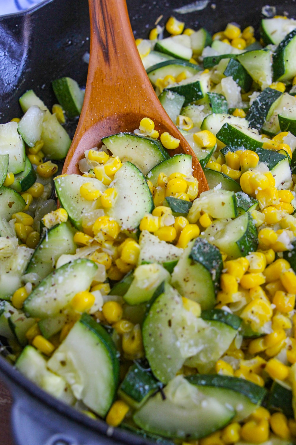 Zucchini and Corn in a skillet being spooned up in a wooden spoon.