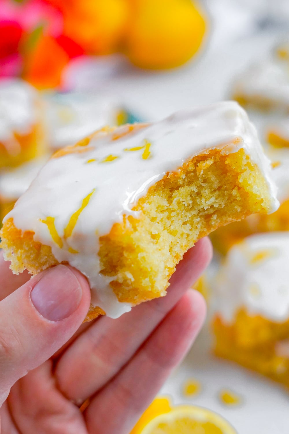 A woman's hand holding a lemon sugar cookie bar with a missing bite.