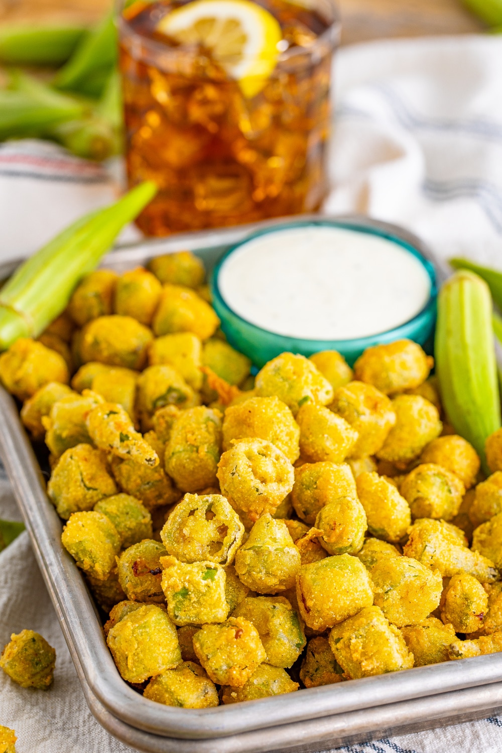 A tray filled with fried okra on a table with a glass of sweet iced tea.