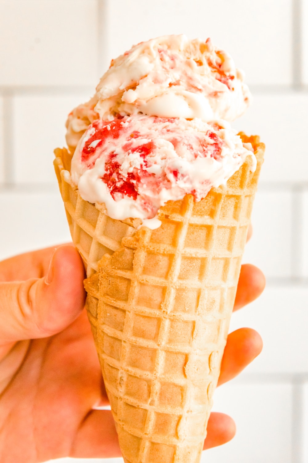 A woman's hand holding a waffle cone filled with Strawberry Ice Cream.