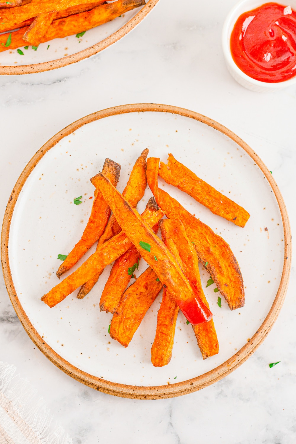 Sweet Potato Fries on white plate. One fry has been dipped in ketchup. 
